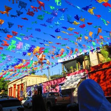 Strings of colorful flags span from building roofs under a bright blue sky